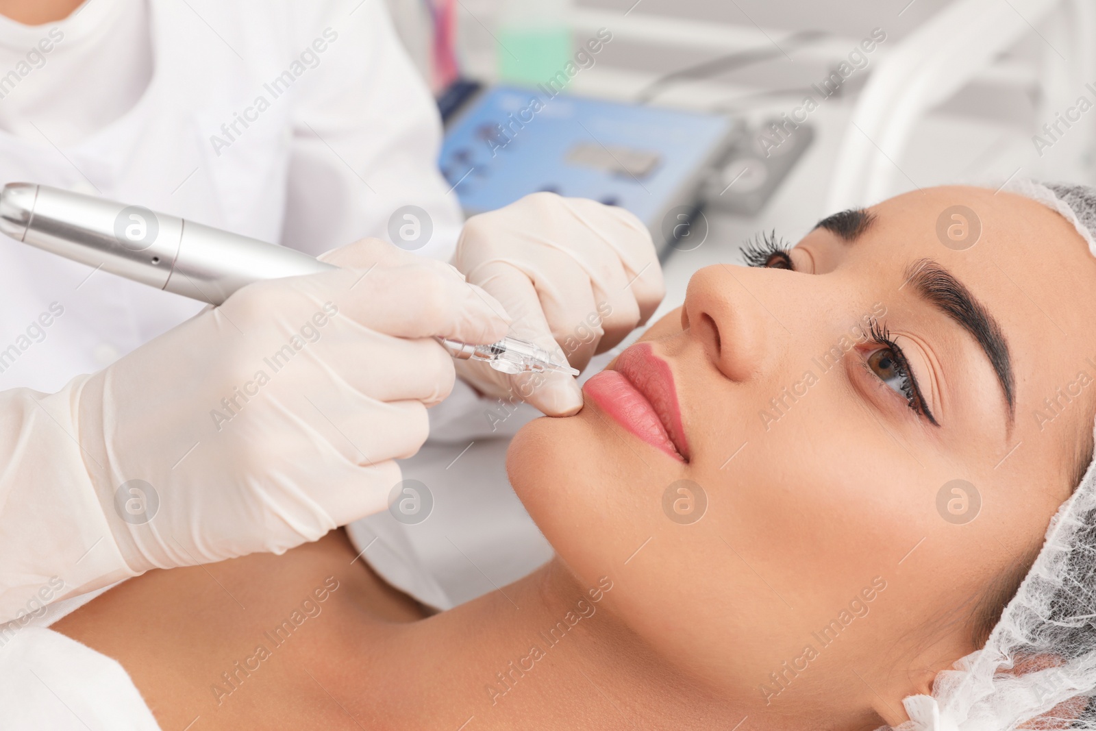 Photo of Young woman undergoing procedure of permanent lip makeup in tattoo salon, closeup