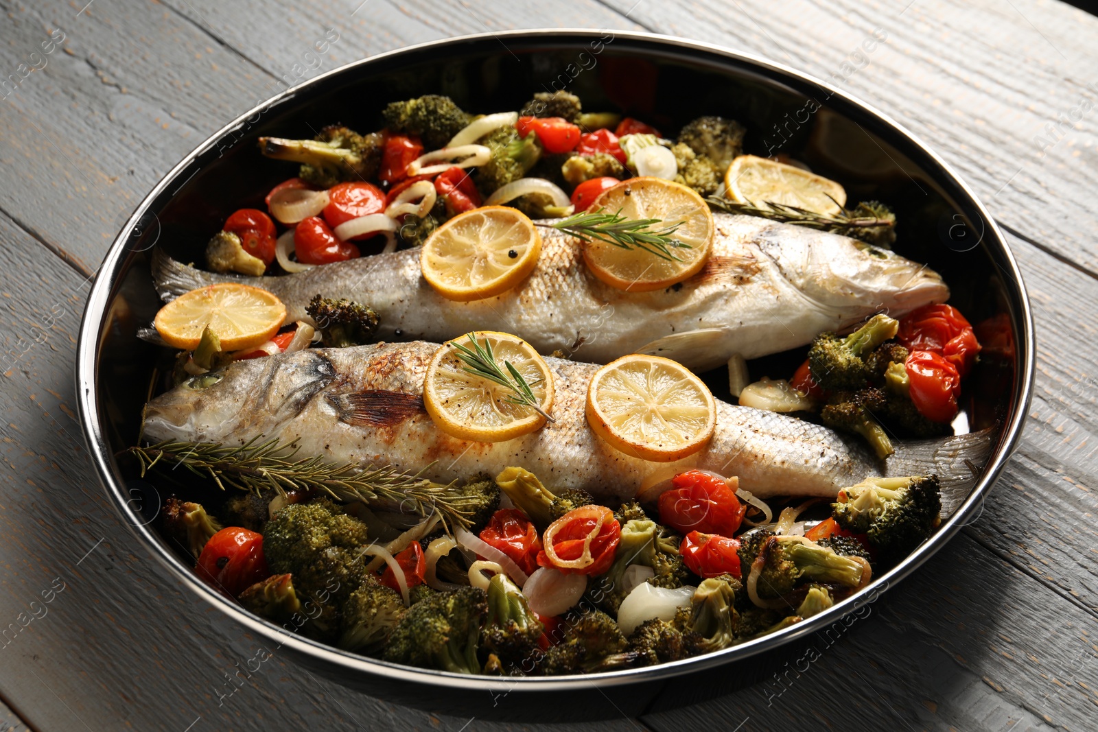 Photo of Baked fish with vegetables, rosemary and lemon on grey wooden table, closeup