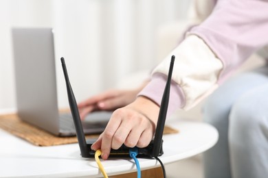Photo of Woman with laptop connecting to internet via Wi-Fi router at table indoors, closeup