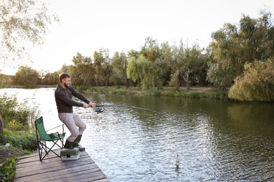 Photo of Man with rod fishing on wooden pier at riverside. Recreational activity