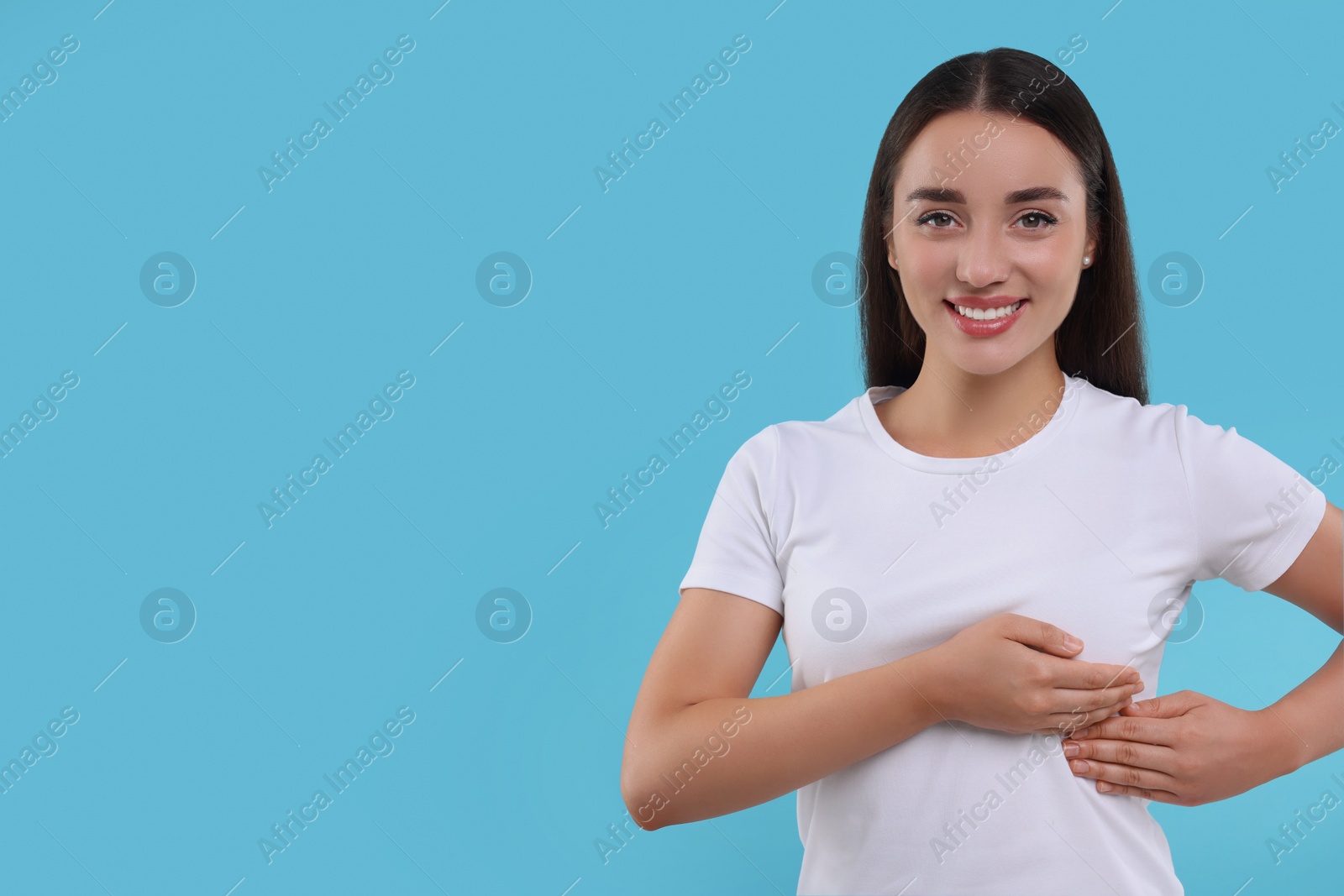 Photo of Beautiful happy woman doing breast self-examination on light blue background, space for text