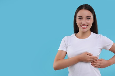 Photo of Beautiful happy woman doing breast self-examination on light blue background, space for text