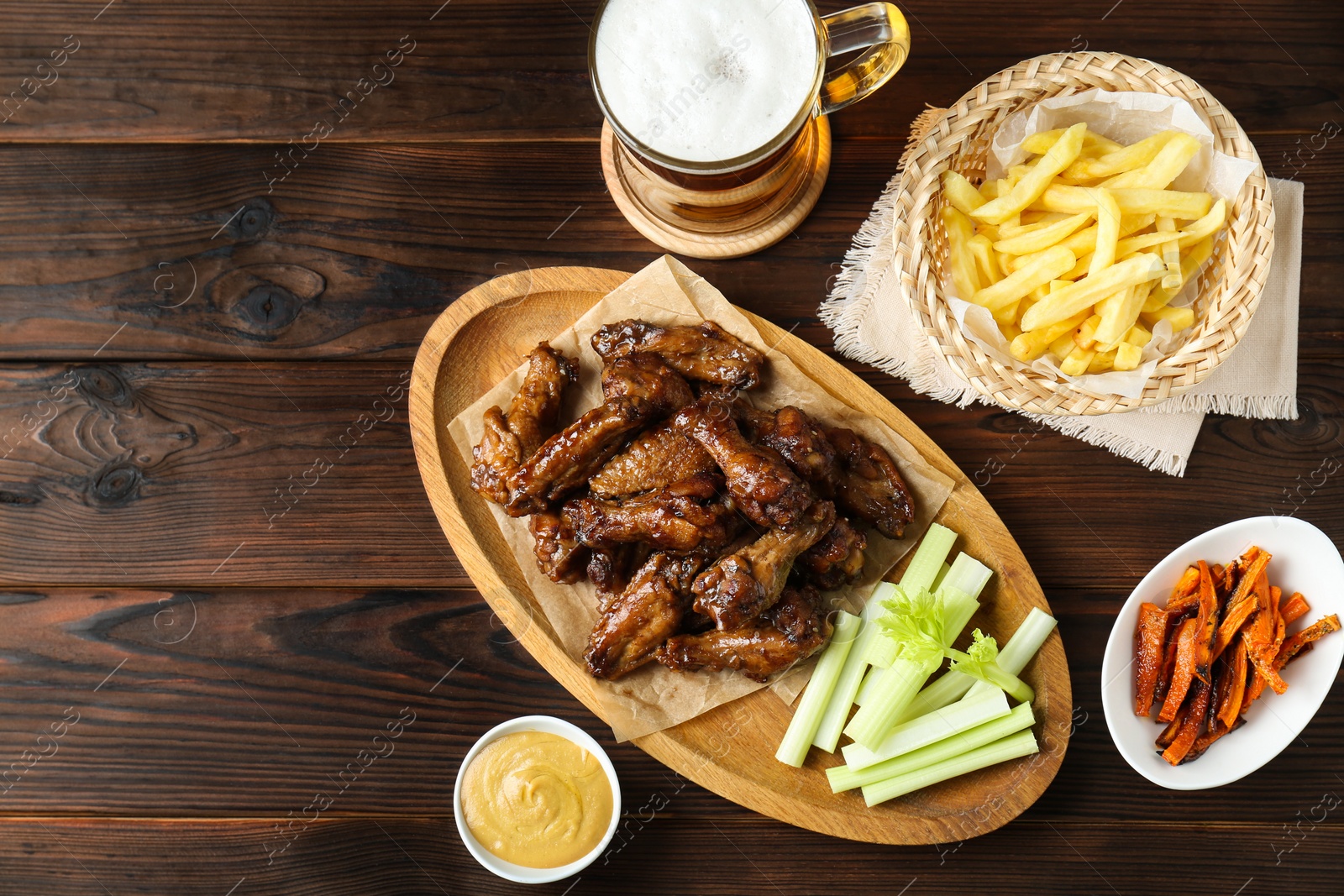 Photo of Delicious chicken wings served with beer on wooden table, flat lay