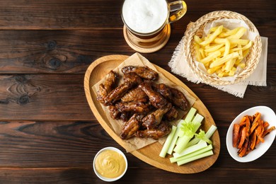 Delicious chicken wings served with beer on wooden table, flat lay