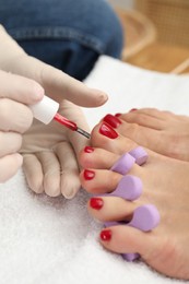 Photo of Pedicurist painting client`s toenails with red polish in beauty salon, closeup