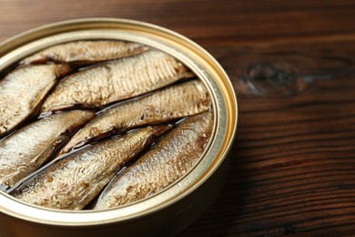 Open tin can of sprats on wooden table, closeup