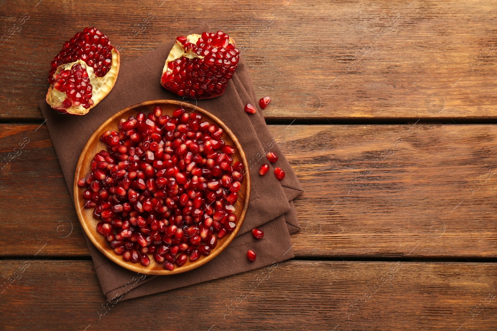 Photo of Ripe juicy pomegranates and grains on wooden table, flat lay. Space for text