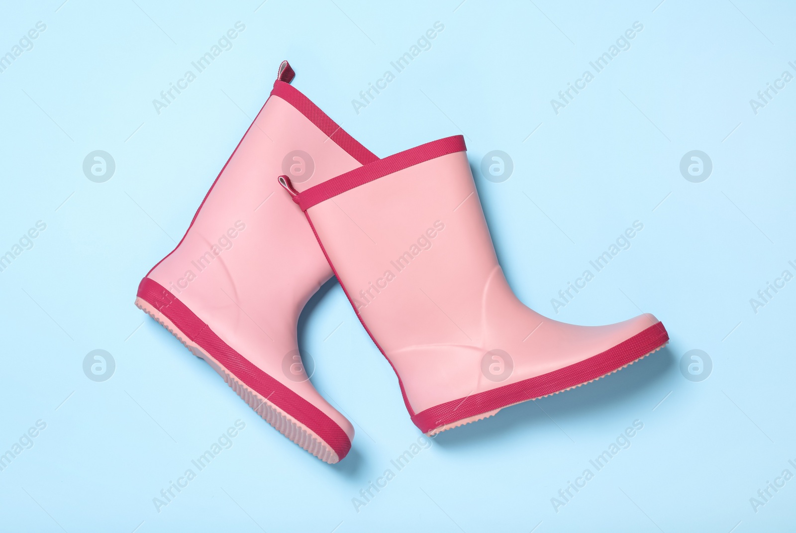 Photo of Pair of pink rubber boots on light blue background, top view