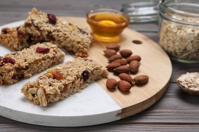 Photo of Tasty granola bars and ingredients on grey wooden table
