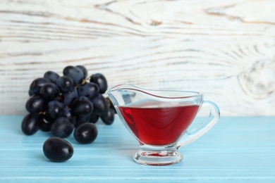 Photo of Glass gravy boat with wine vinegar and fresh grapes on wooden table