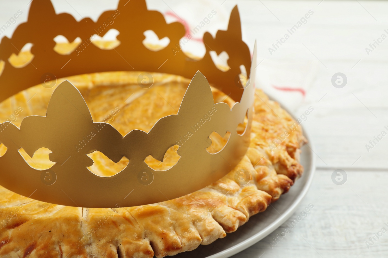 Photo of Traditional galette des Rois with paper crown on white wooden table, closeup