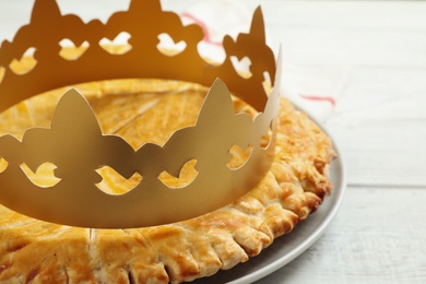 Traditional galette des Rois with paper crown on white wooden table, closeup
