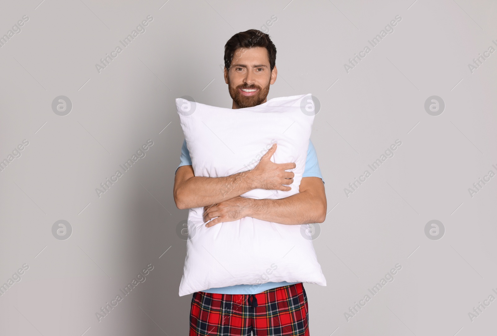 Photo of Smiling handsome man hugging soft pillow on light grey background