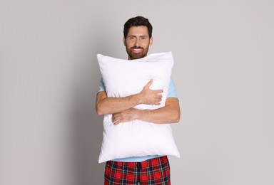Smiling handsome man hugging soft pillow on light grey background