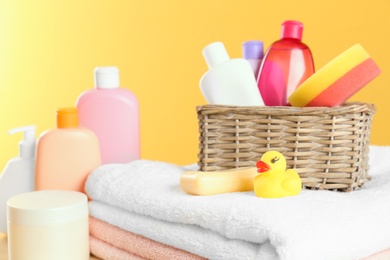 Photo of Wicker basket with baby cosmetic products, toy and towels against color background, closeup