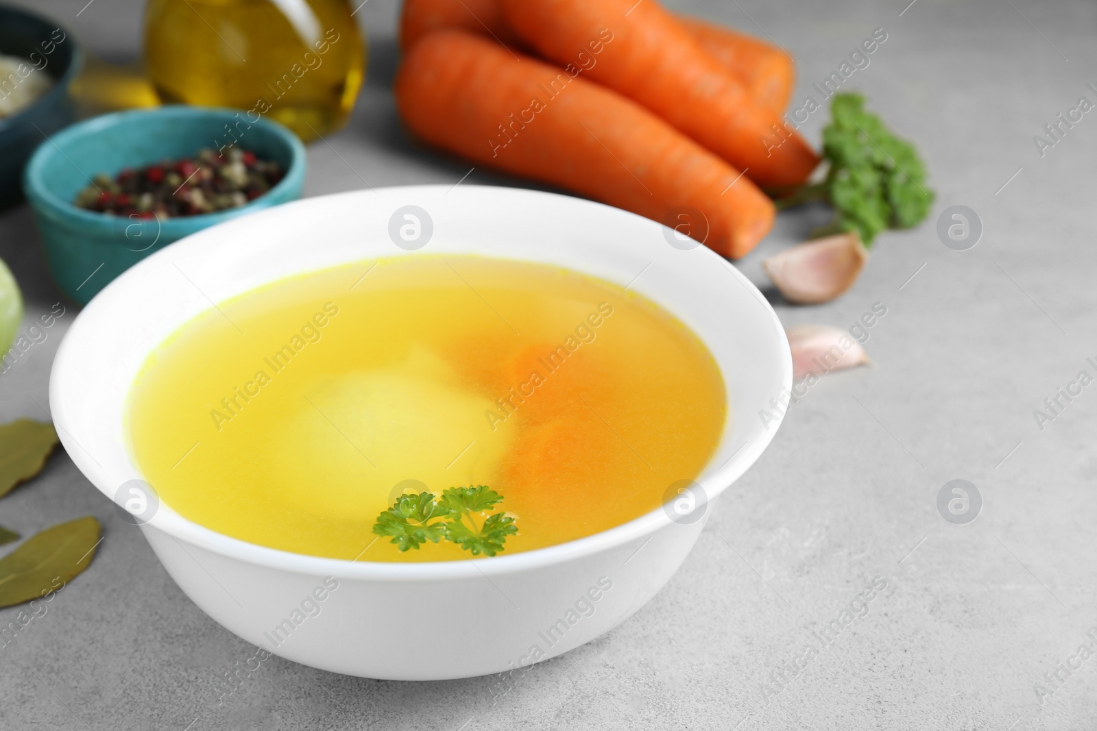 Photo of Delicious chicken bouillon and ingredients on light grey textured table, closeup