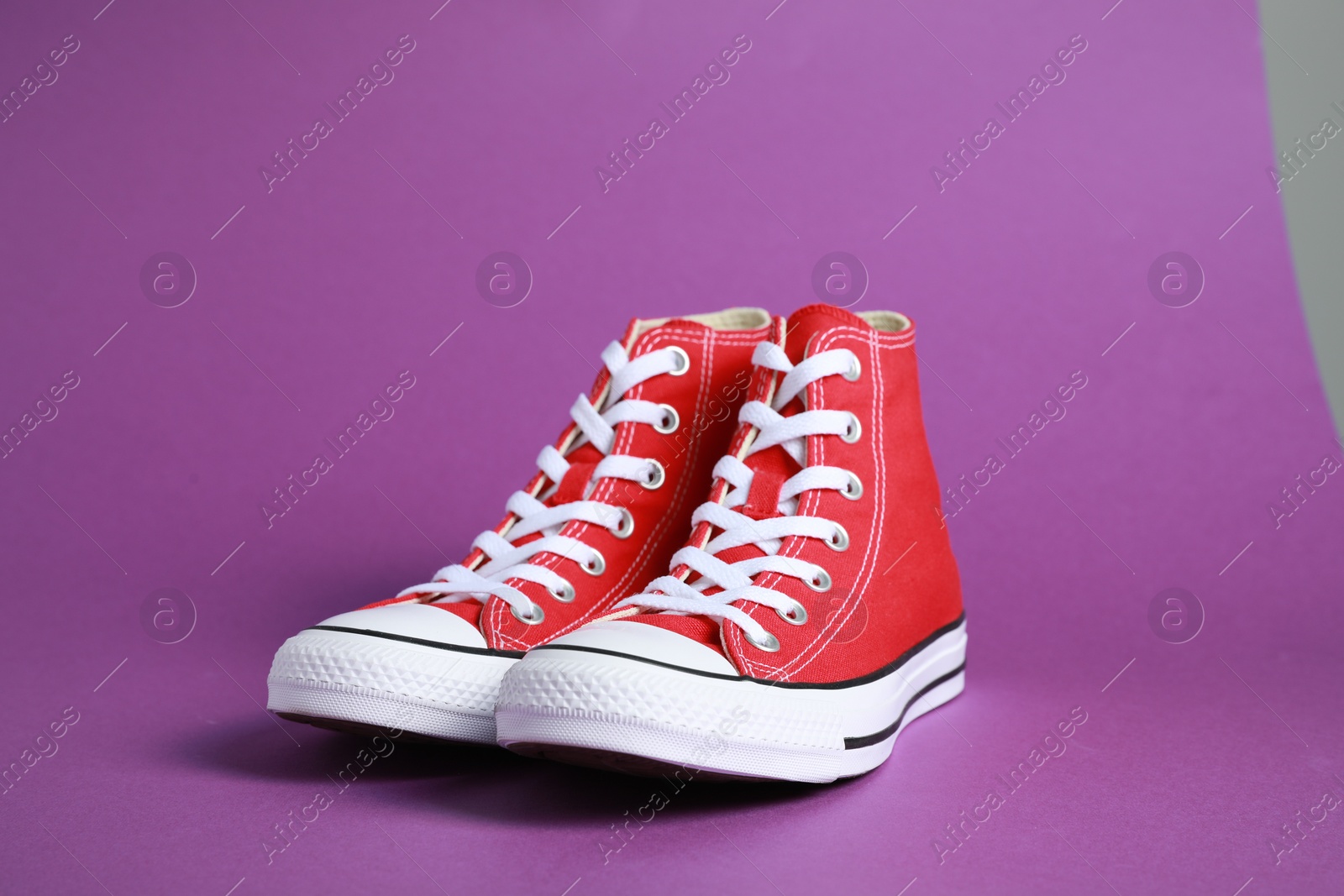 Photo of Pair of new stylish red sneakers on purple background