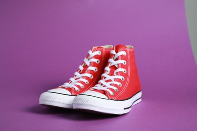 Pair of new stylish red sneakers on purple background