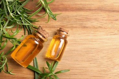 Photo of Bottles of essential oil and fresh rosemary sprigs on wooden table, flat lay. Space for text