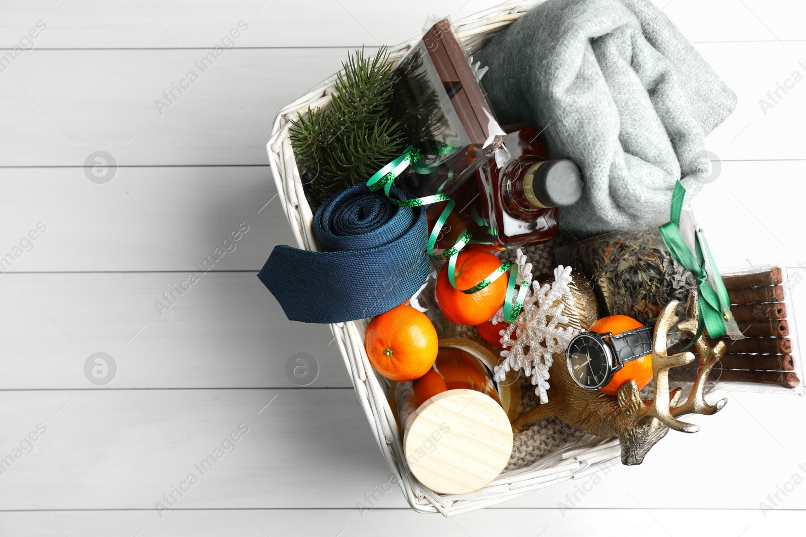 Photo of Wicker basket with Christmas gift set on white wooden table, top view. Space for text