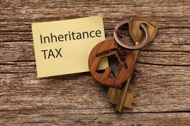 Photo of Inheritance Tax. Paper note and key with key chain in shape of house on wooden table, flat lay