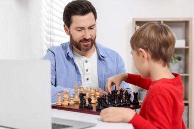 Photo of Father and son playing chess following online lesson in room