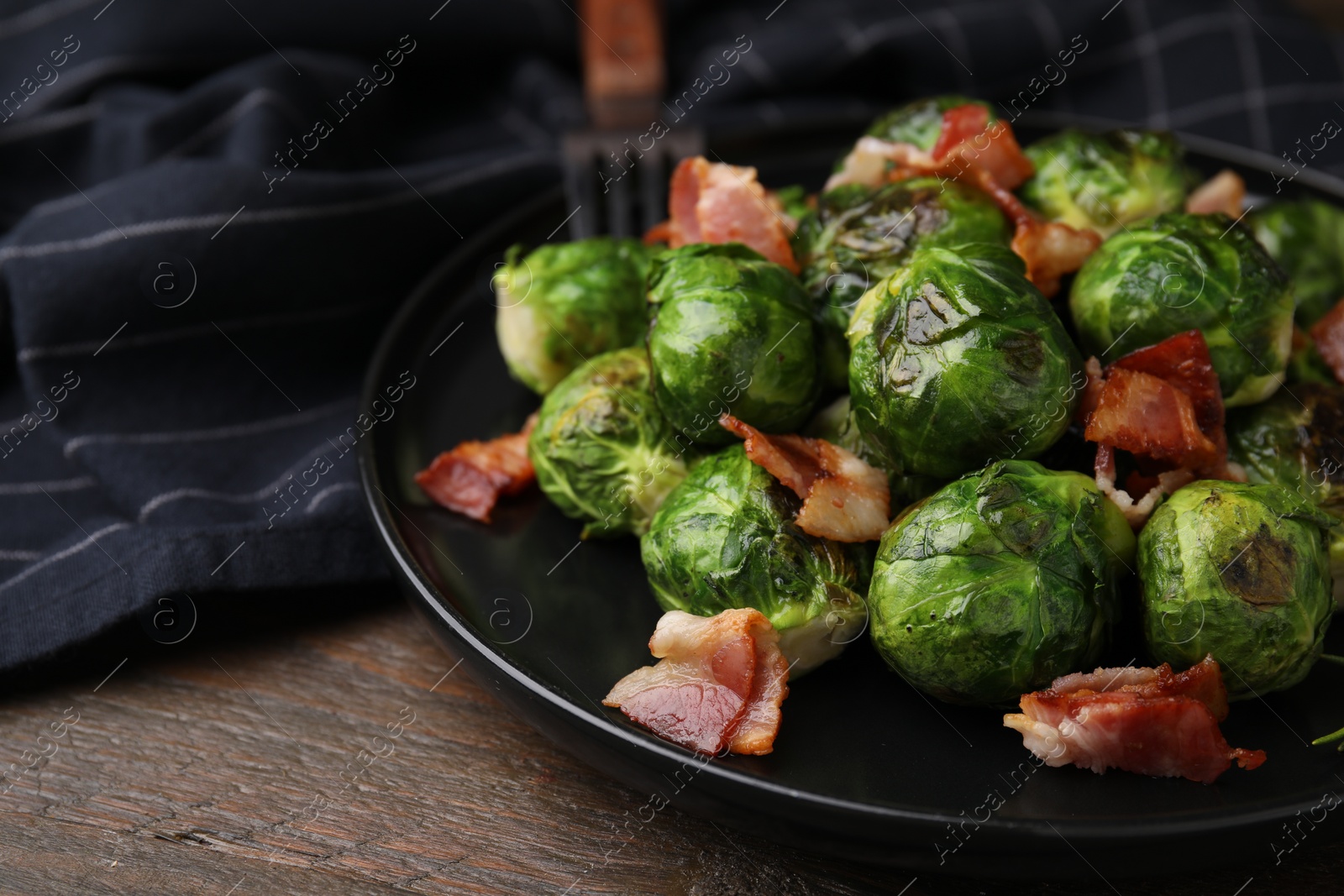 Photo of Delicious roasted Brussels sprouts and bacon on wooden table, closeup. Space for text