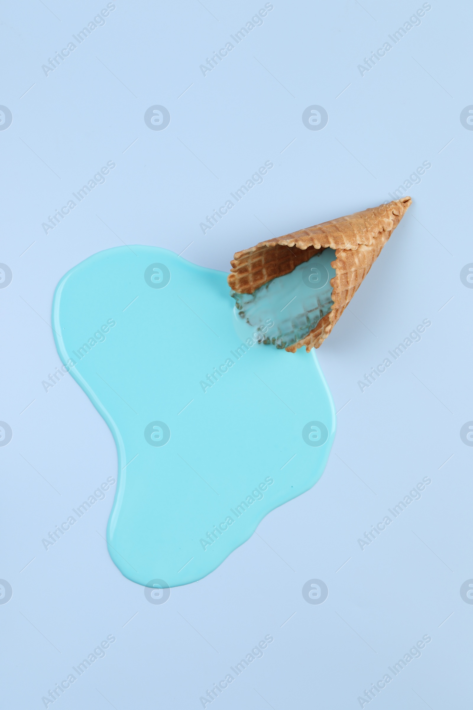 Photo of Melted ice cream and wafer cone on light blue background, top view