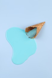 Photo of Melted ice cream and wafer cone on light blue background, top view