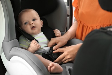 Mother fastening baby to child safety seat inside of car