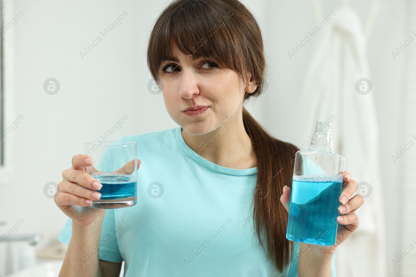 Photo of Young woman using mouthwash in bathroom. Oral hygiene