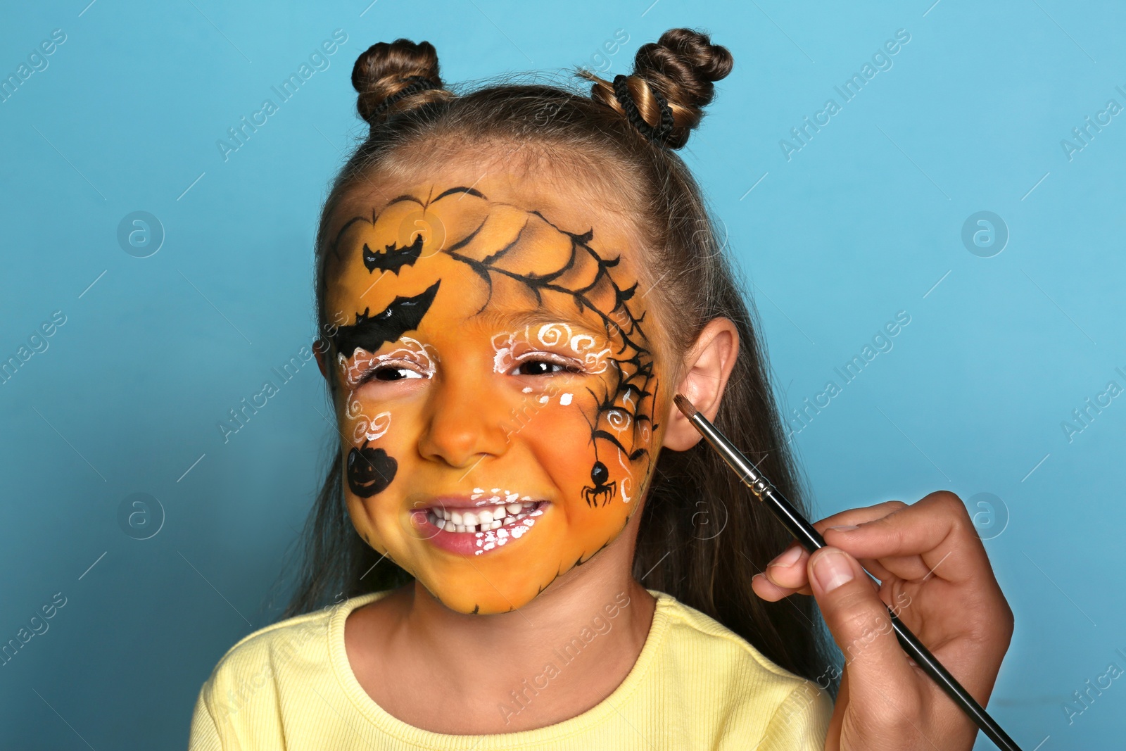 Photo of Artist painting face of little girl on blue background