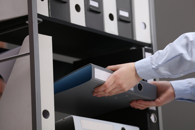 Photo of Woman taking folder with documents from shelf in office, closeup