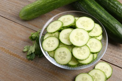 Photo of Cut cucumber in glass bowl, fresh vegetables and parsley on wooden table, closeup