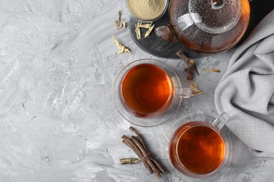 Aromatic licorice tea, dried sticks of licorice root and powder on light gray textured table, flat lay. Space for text