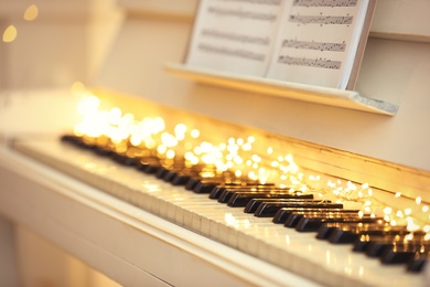 Photo of White piano with fairy lights and note sheets closeup. Christmas music