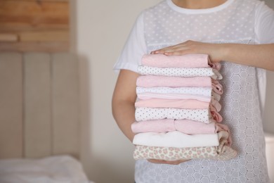 Photo of Woman holding stack of girl's clothes in bedroom, closeup. Space for text