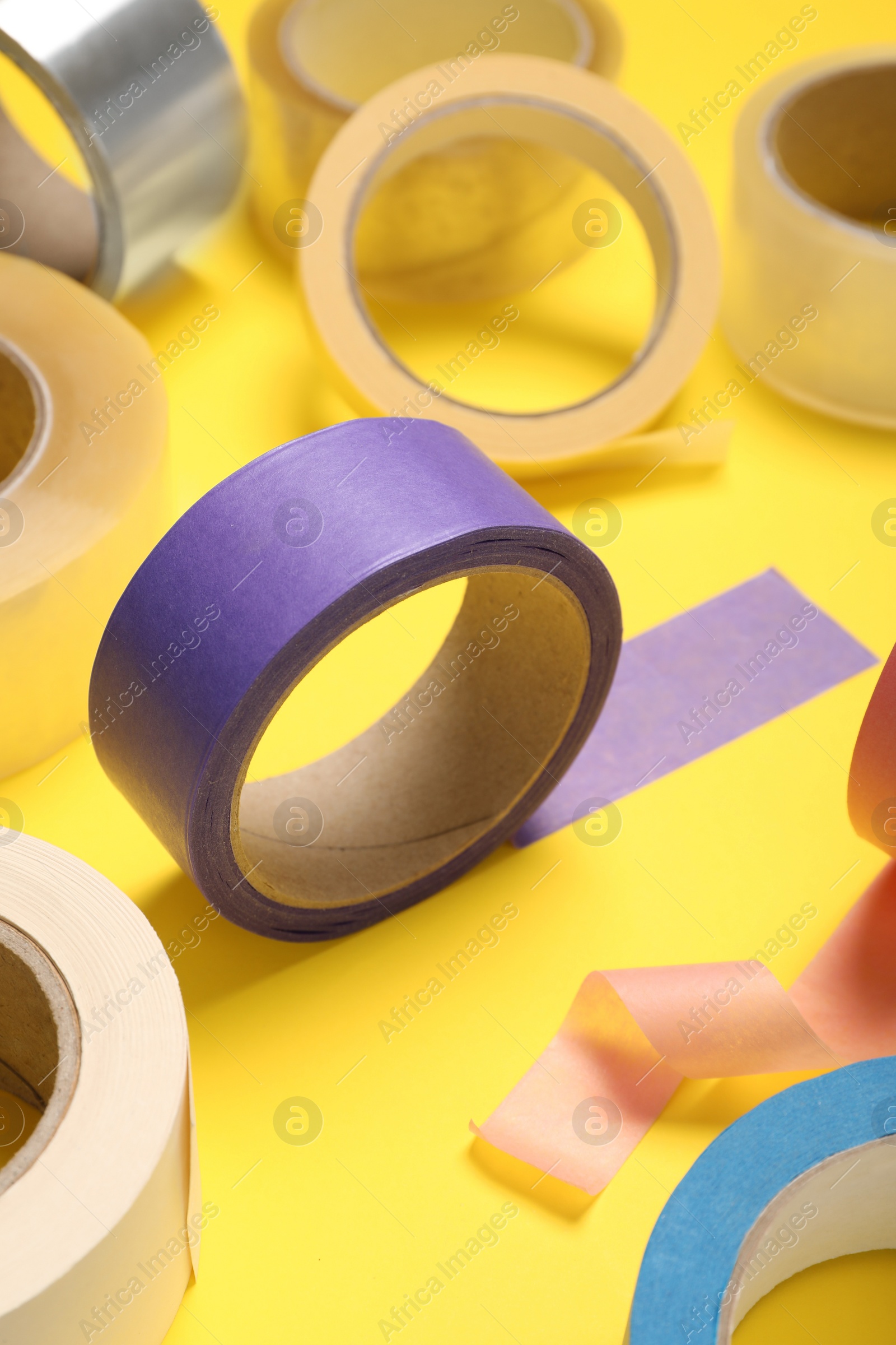 Photo of Many rolls of bright adhesive tape on yellow background