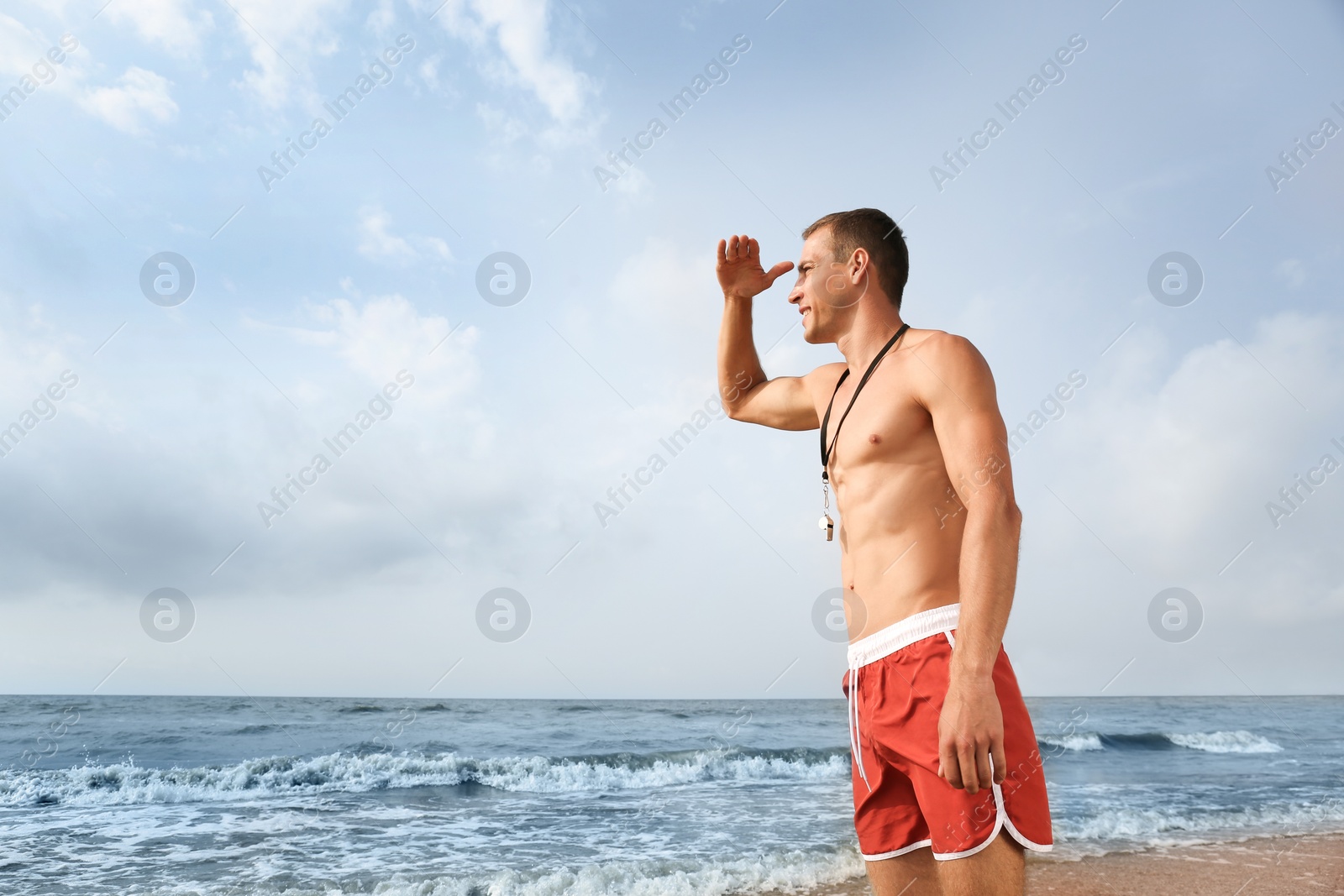 Photo of Handsome lifeguard with whistle near sea on summer day