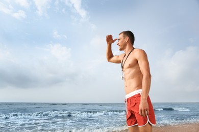 Photo of Handsome lifeguard with whistle near sea on summer day