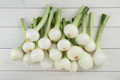 Whole green spring onions on white wooden table, flat lay