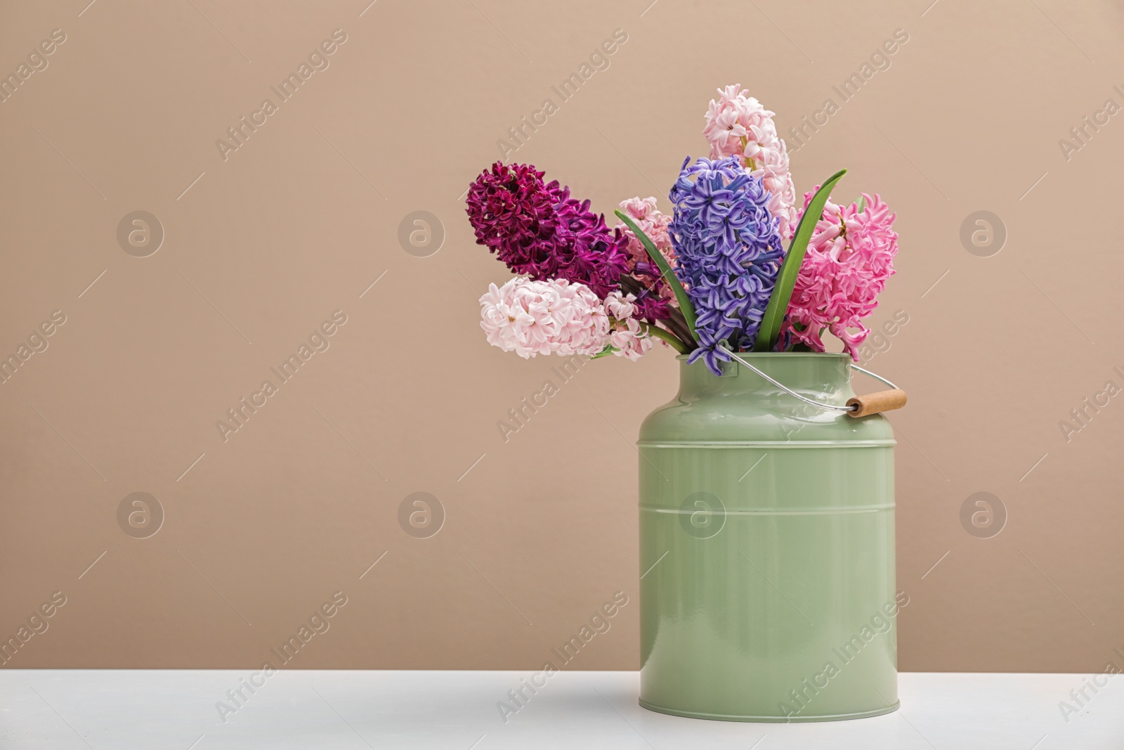 Photo of Beautiful hyacinths in metal can on table against color background, space for text. Spring flowers