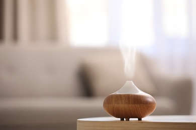 Photo of Modern essential oil diffuser on table indoors. Space for text