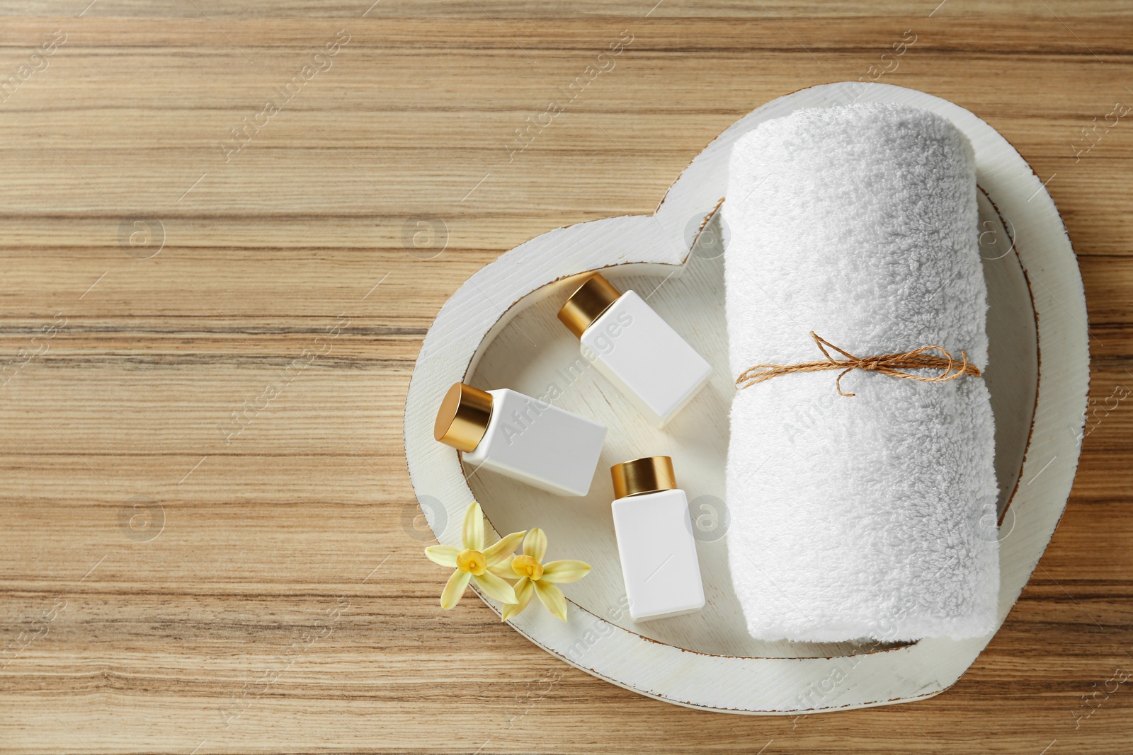 Photo of Top view of heart shaped tray with towel and cosmetic bottles on wooden table, space for text. Spa treatment