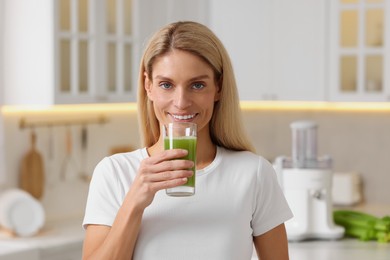 Photo of Happy woman with glass of fresh celery juice in kitchen