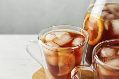 Cups and jug of refreshing iced tea on light table