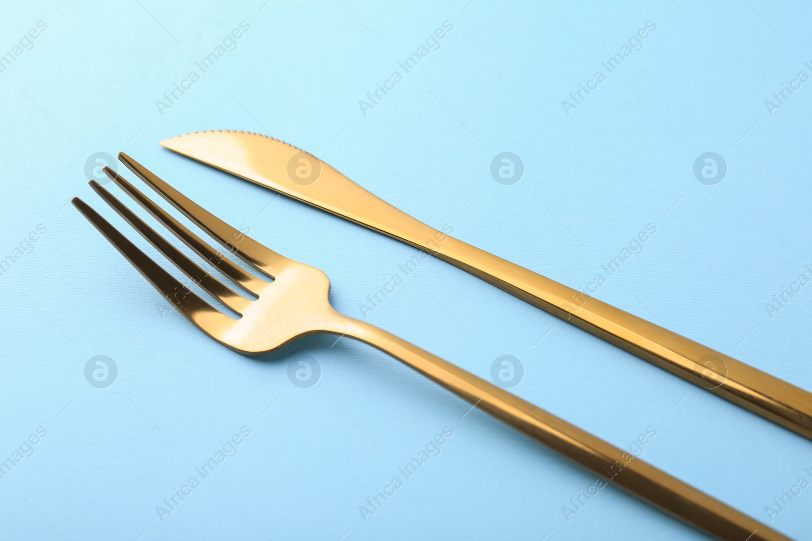Photo of Stylish cutlery. Golden knife and fork on light blue background, closeup