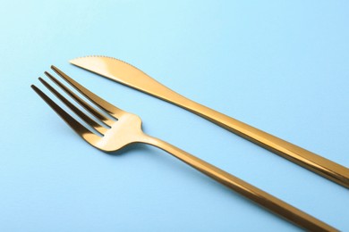 Stylish cutlery. Golden knife and fork on light blue background, closeup