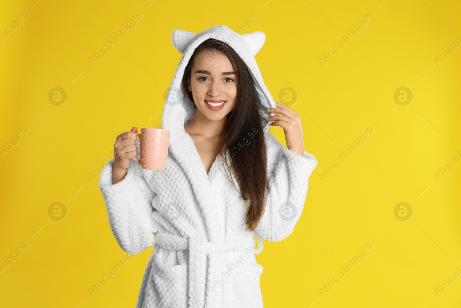 Photo of Young woman in bathrobe with cup of coffee on yellow background