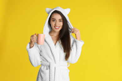 Photo of Young woman in bathrobe with cup of coffee on yellow background